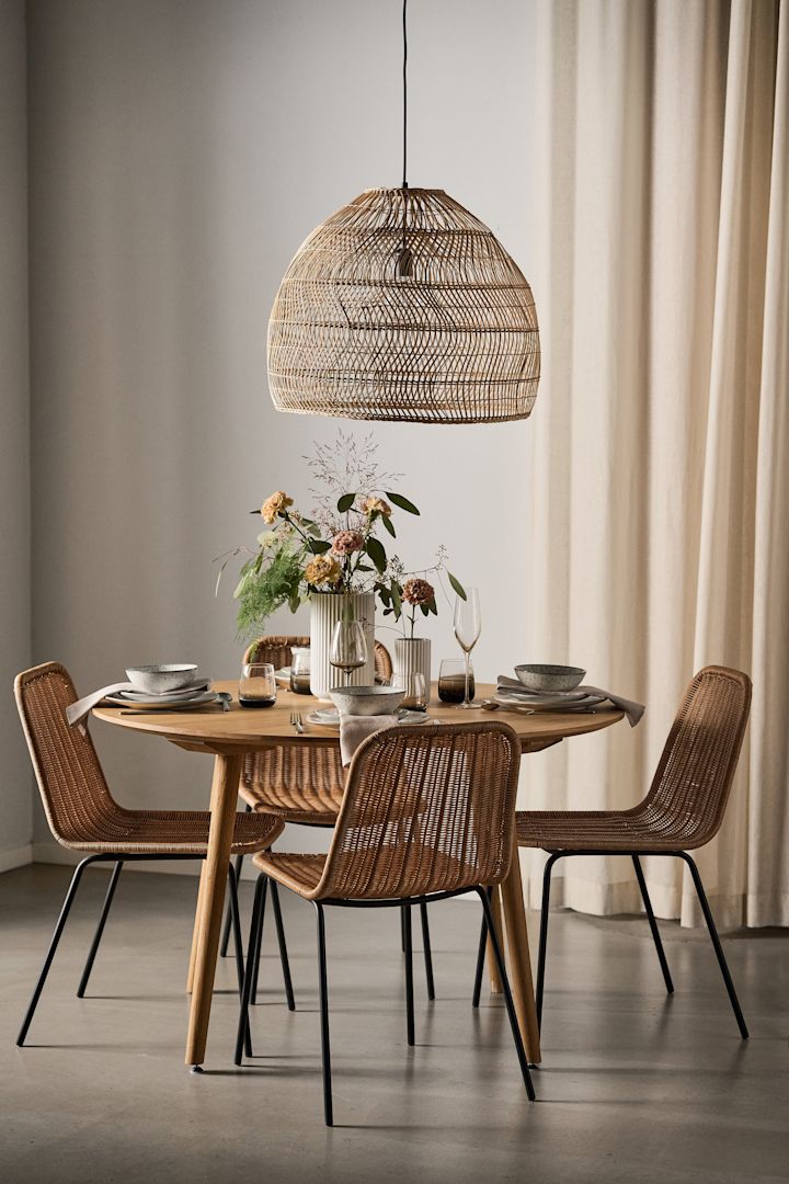 Un comedor de estilo boho con una lámpara de rafia y una mesa redonda con cuatro sillas Hapur de House Doctor a su alrededor.