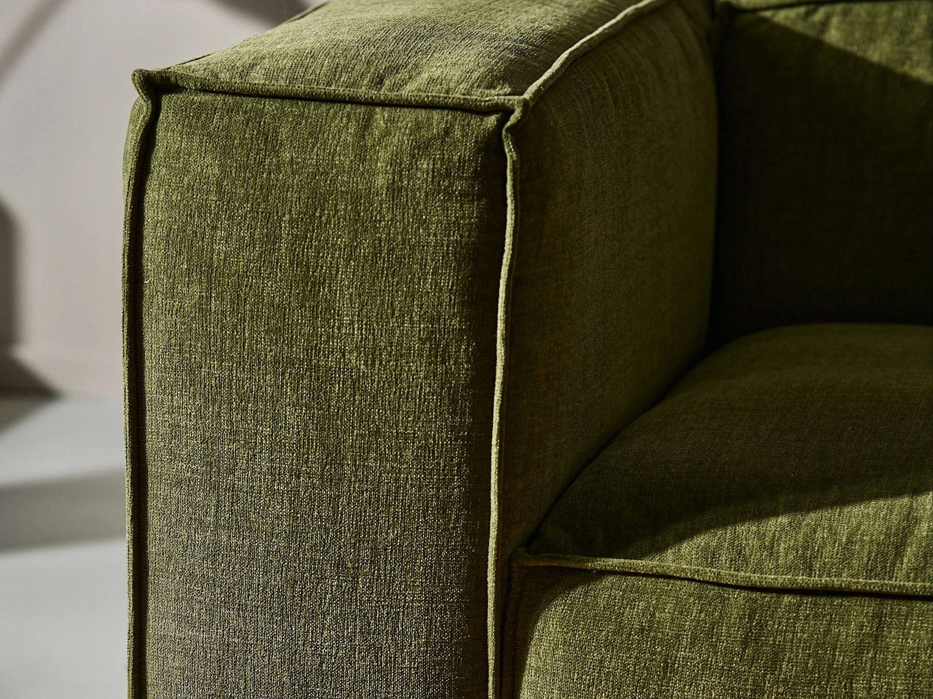 Primer plano del reposabrazos de un sofá de tela verde con textura y ribetes visibles.