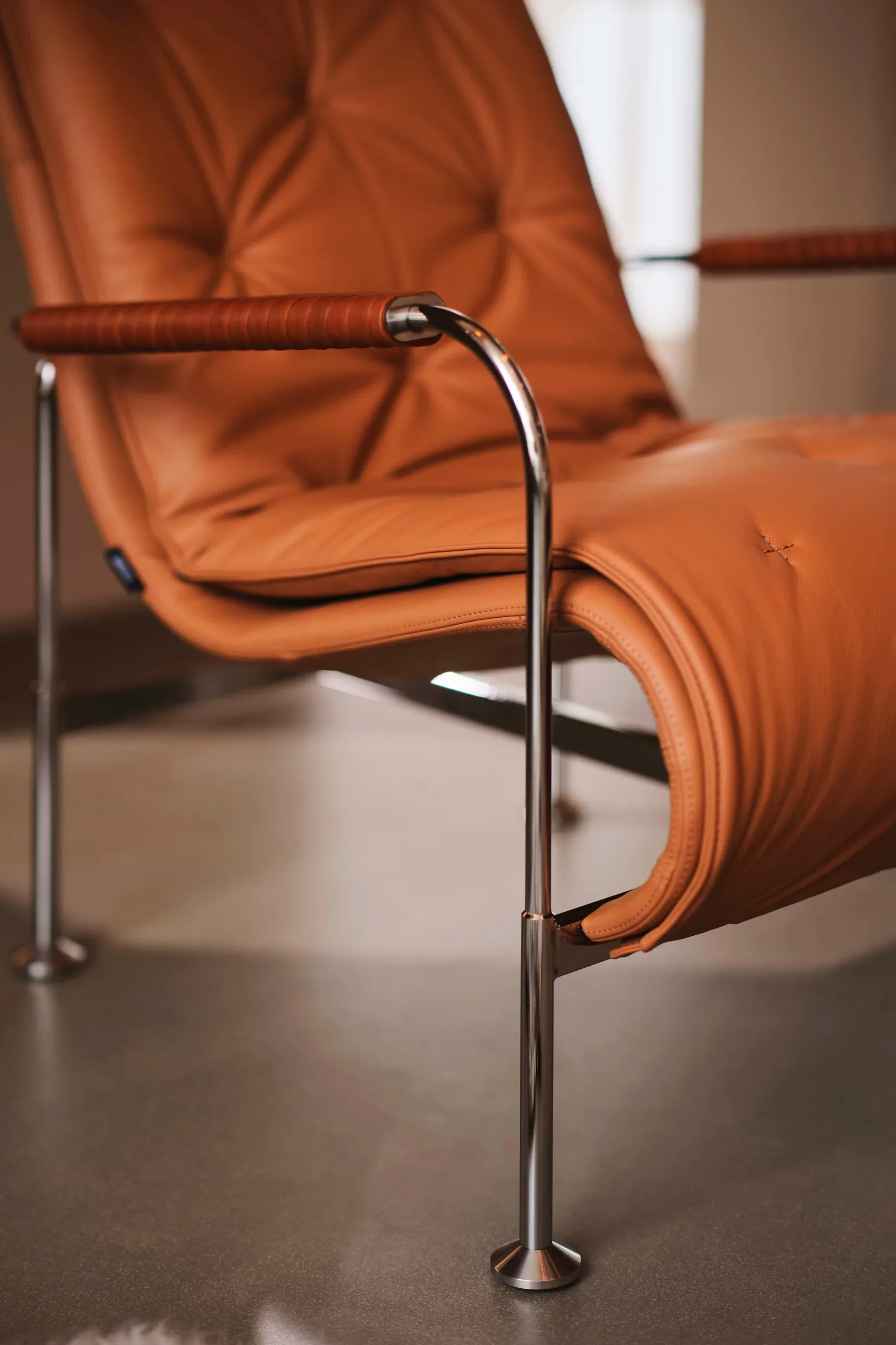 Sillón de cuero marrón claro con estructura cromada y reposabrazos revestidos.