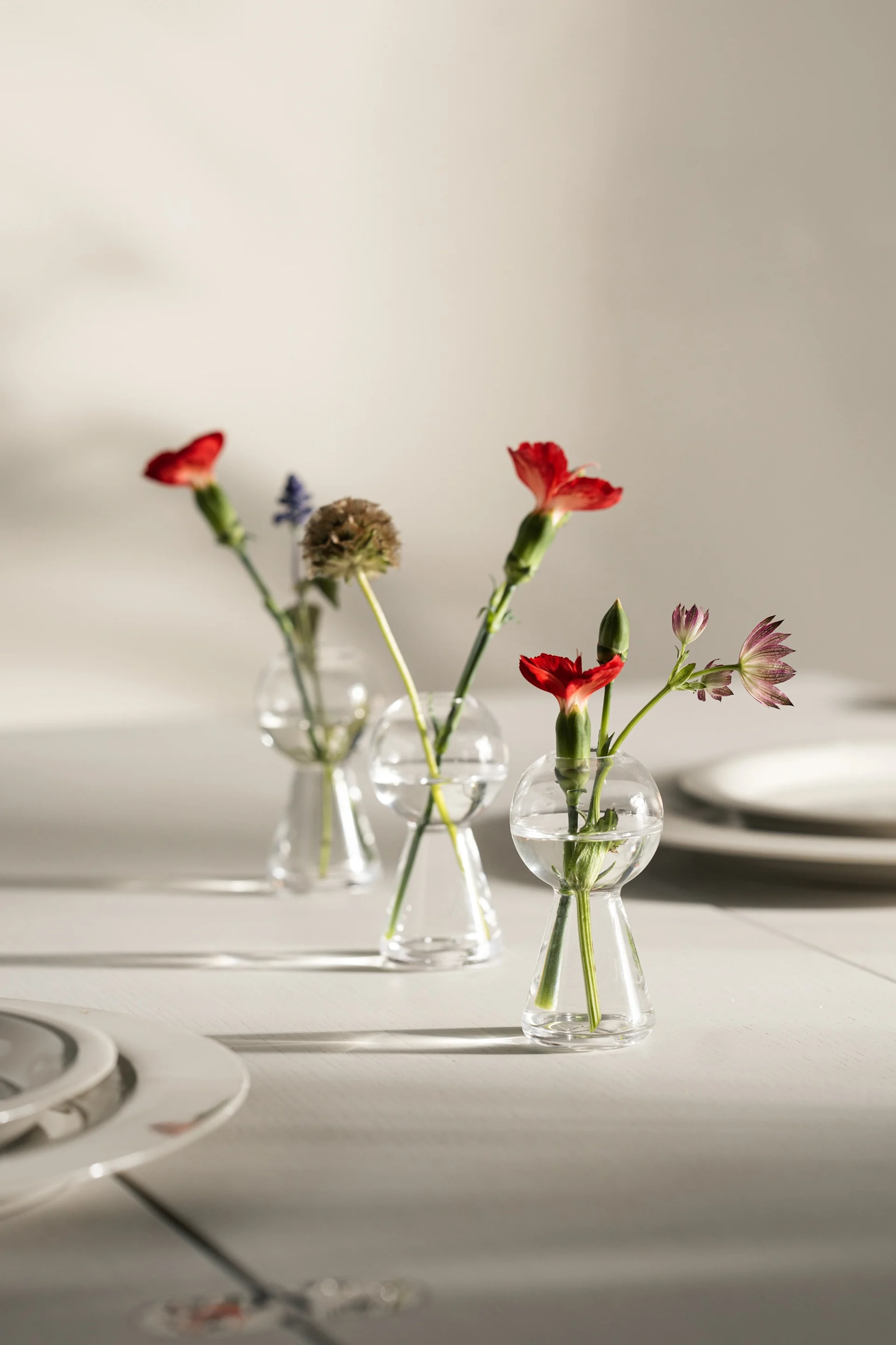 En una mesa puesta se encuentran tres mini jarrones con flores sueltas de Design House Stockholm.