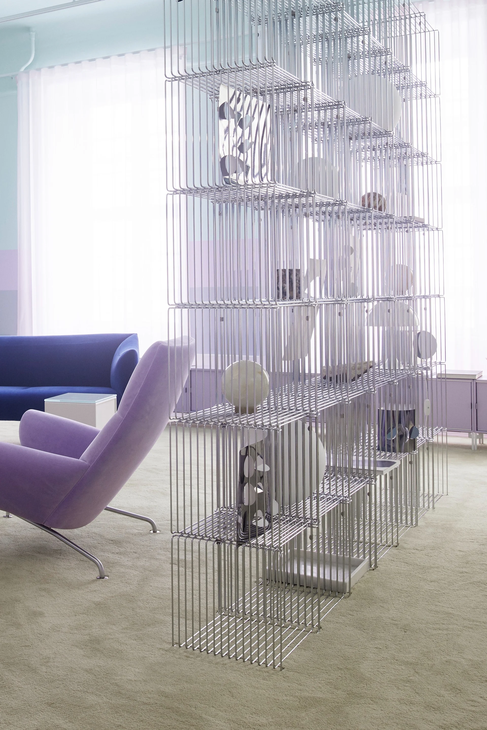 Habitación moderna con una alta estantería de alambre plateado como separador, un sillón morado y un sofá azul.