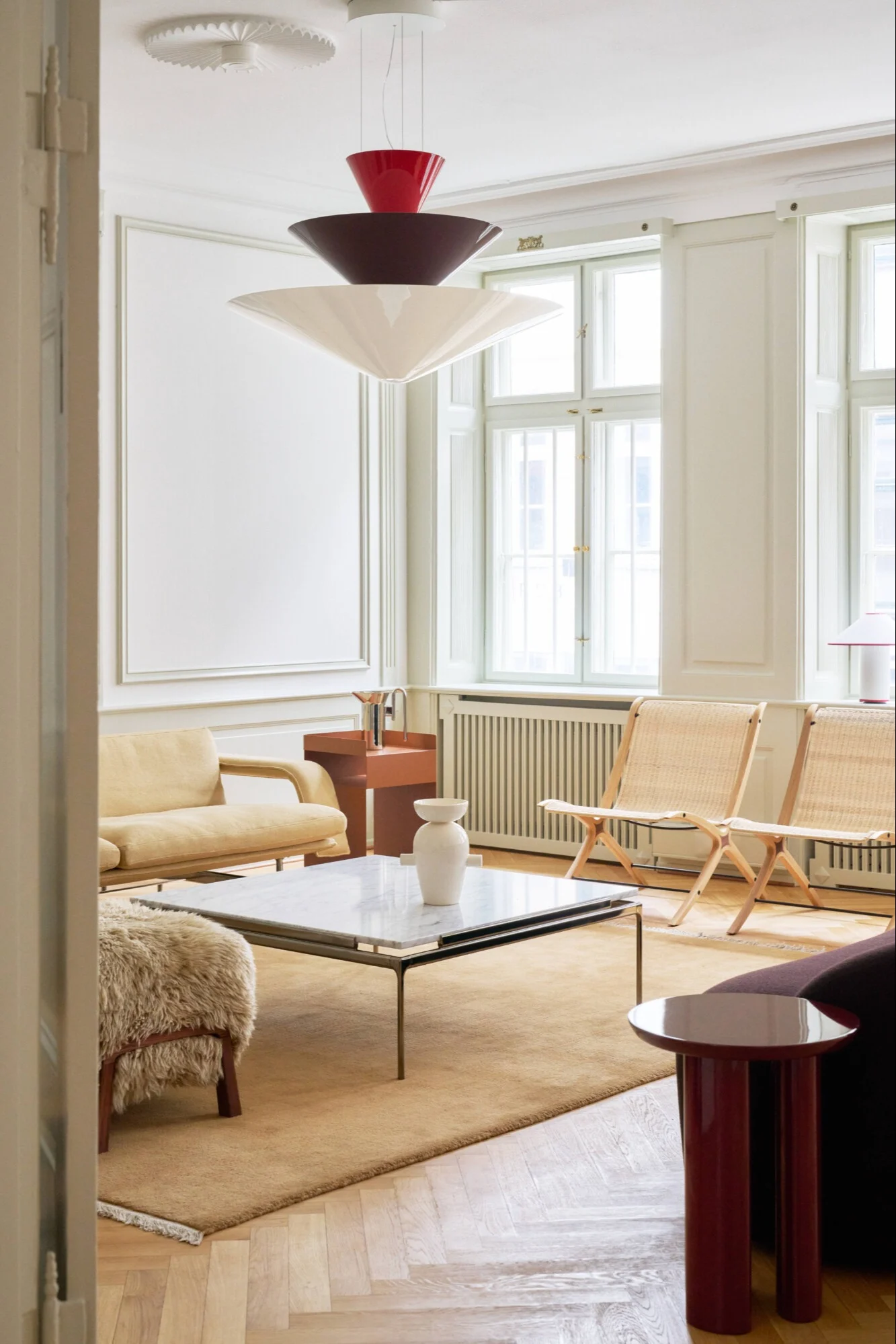 Un salón contemporáneo con una lámpara colgante escalonada, sofá amarillo claro, sillas de caña y mesa de centro de mármol.