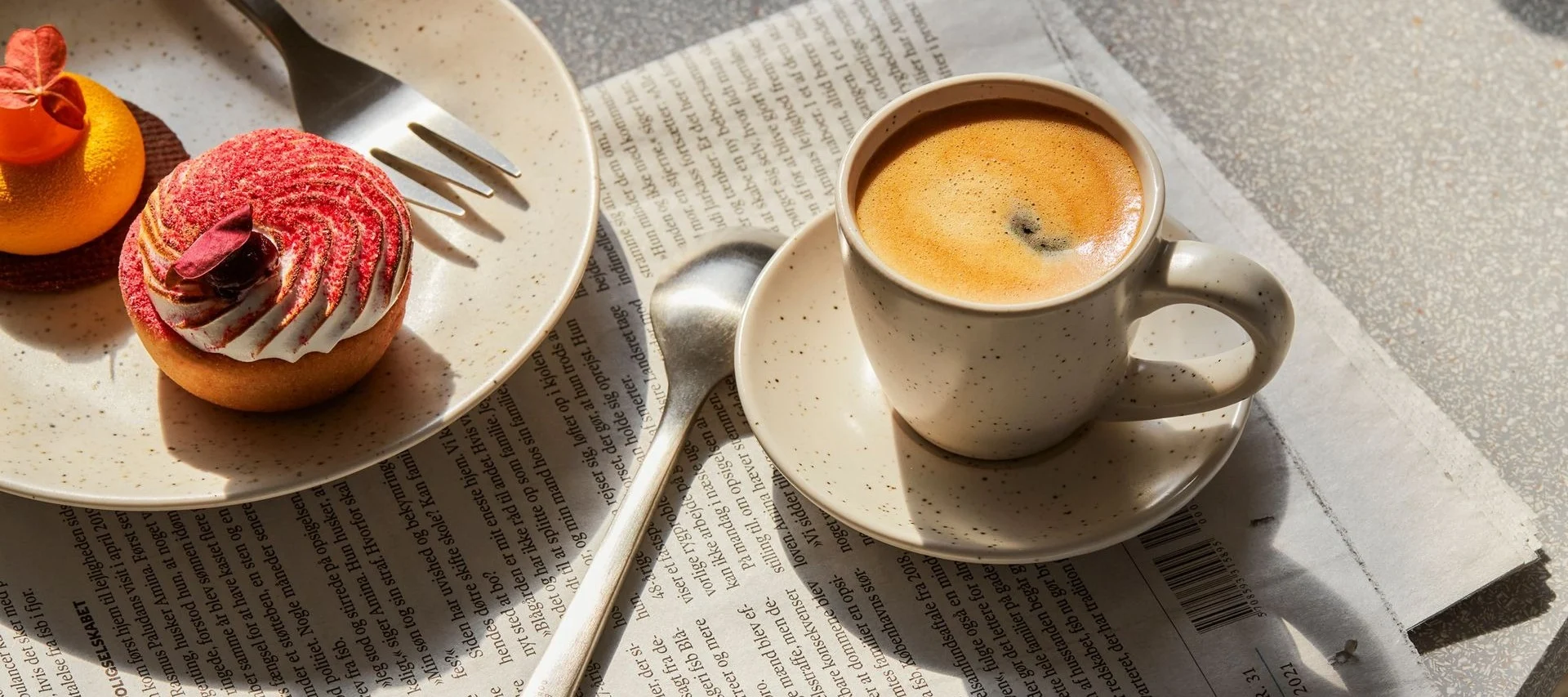 Taza de café y dos pasteles, una tarta roja y una naranja, sobre un periódico.