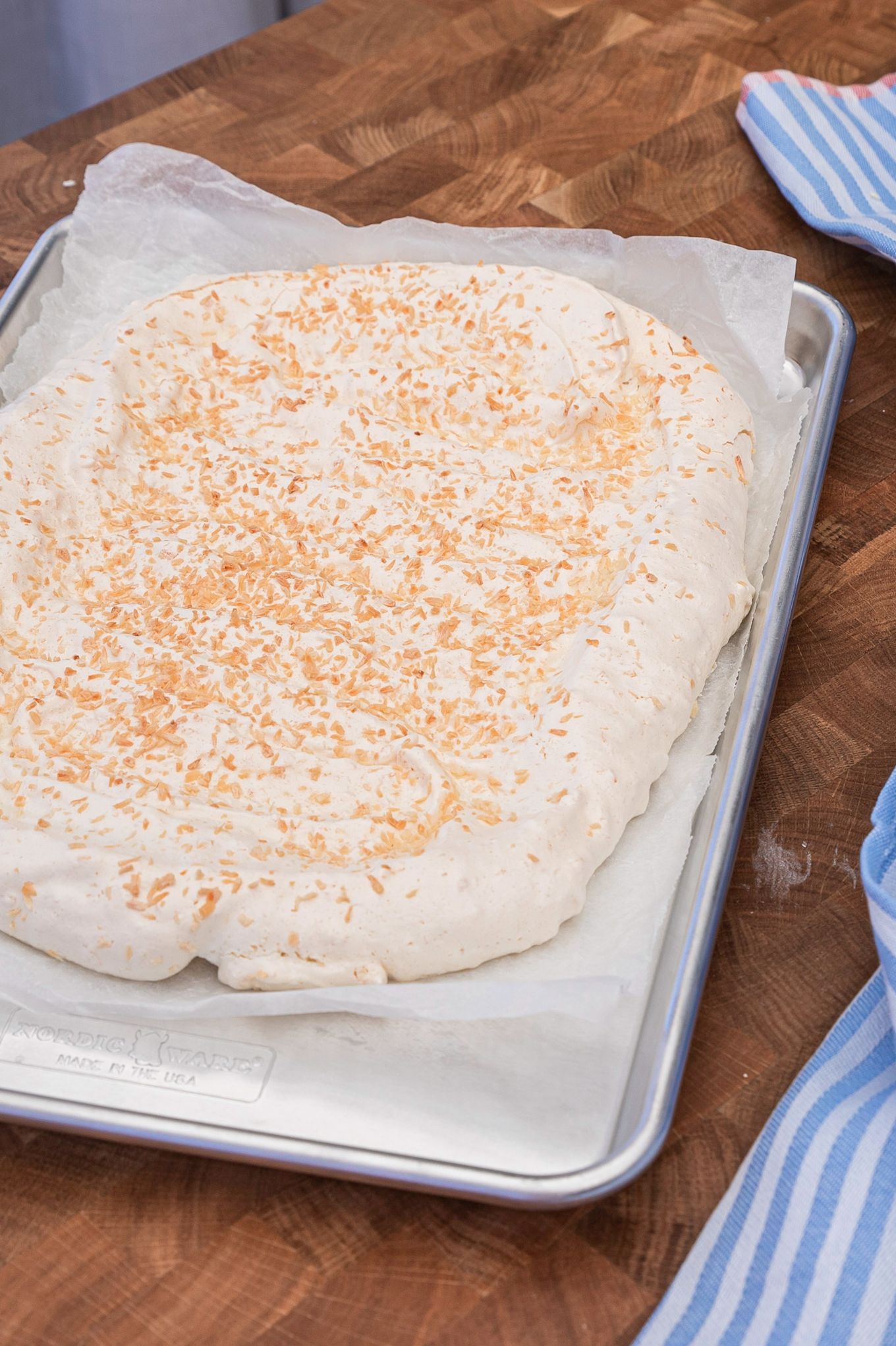 Hornea una deliciosa tarta de merengue con la sencilla receta de tarta de Pascua de Baka med Frida en una bandeja para hornear de Nordic Ware. Espolvorea coco sobre la base de merengue para darle un toque crujiente.