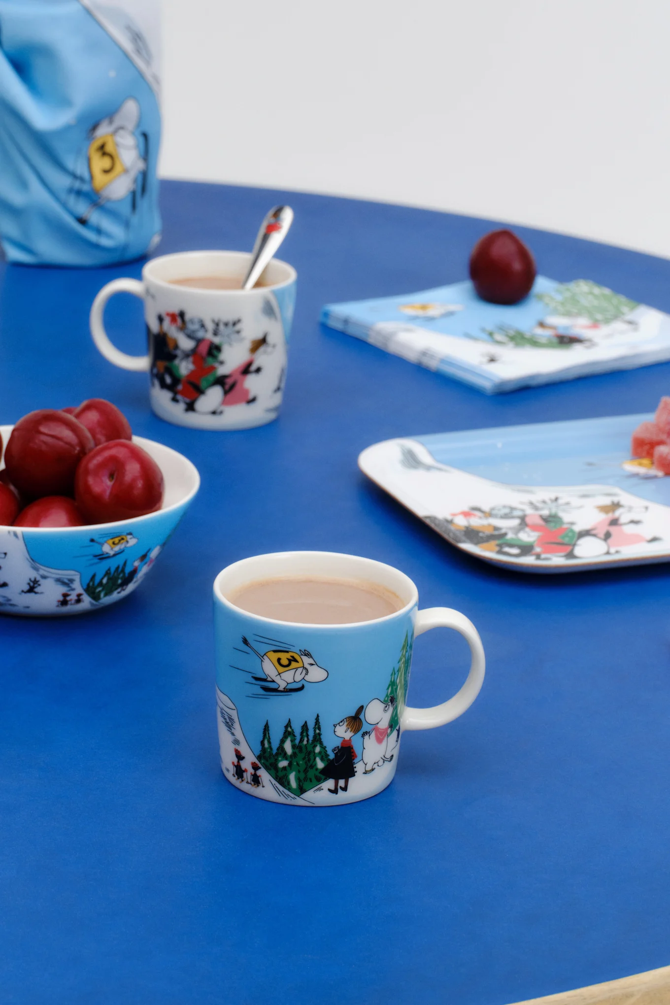 La taza Mumin del invierno 2024, "Salto de esquí", está sobre una mesa decorada en azul.