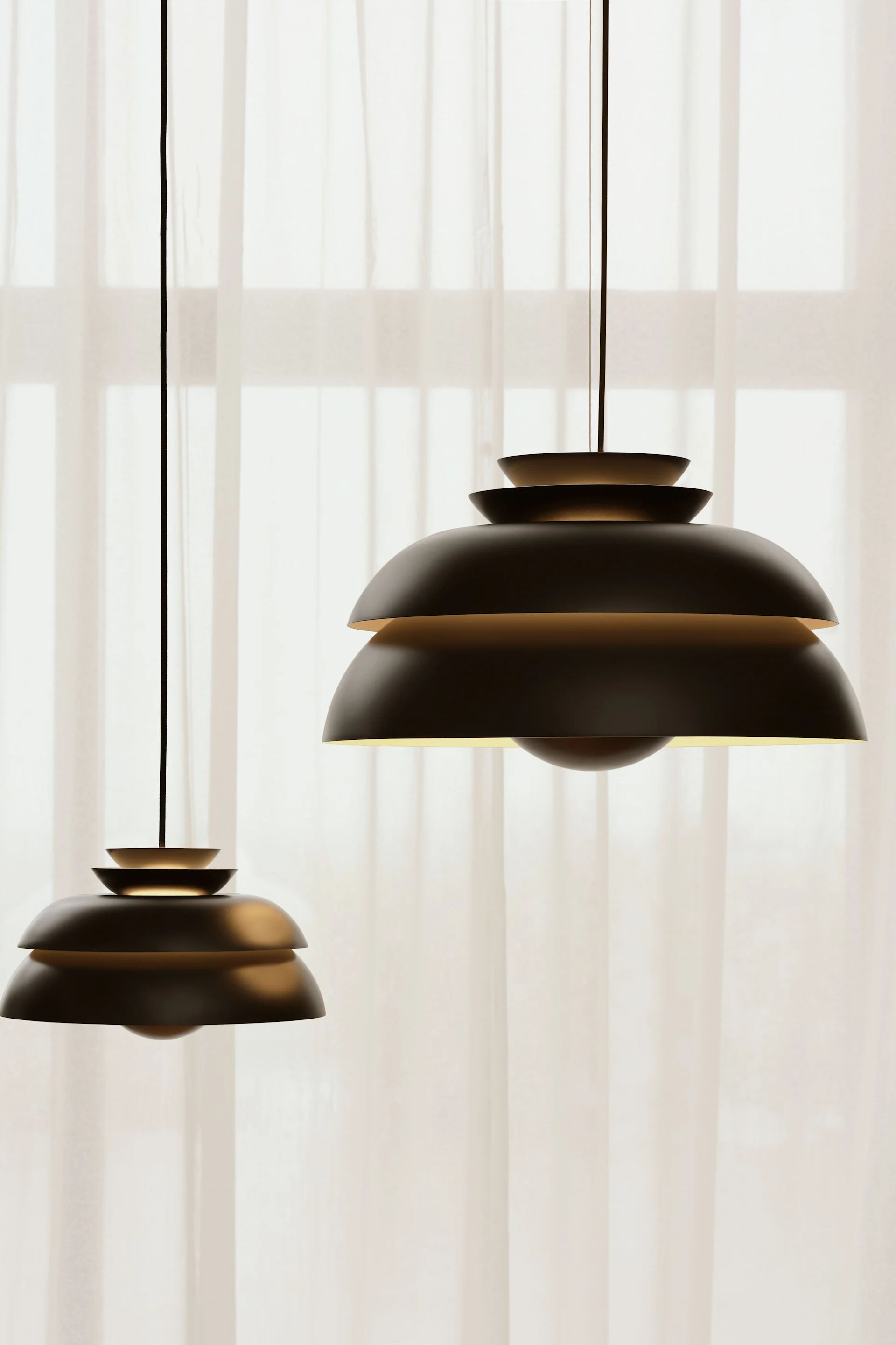 La lámpara colgante Concert en negro de Fritz Hansen está situada frente a una ventana con cortinas.