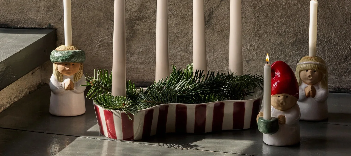 La decoración navideña de este año, 2026, es alegre y nostálgica. Un portavelas a rayas rojas está rodeado de pequeños portavelas con forma de cantantes de villancicos. 