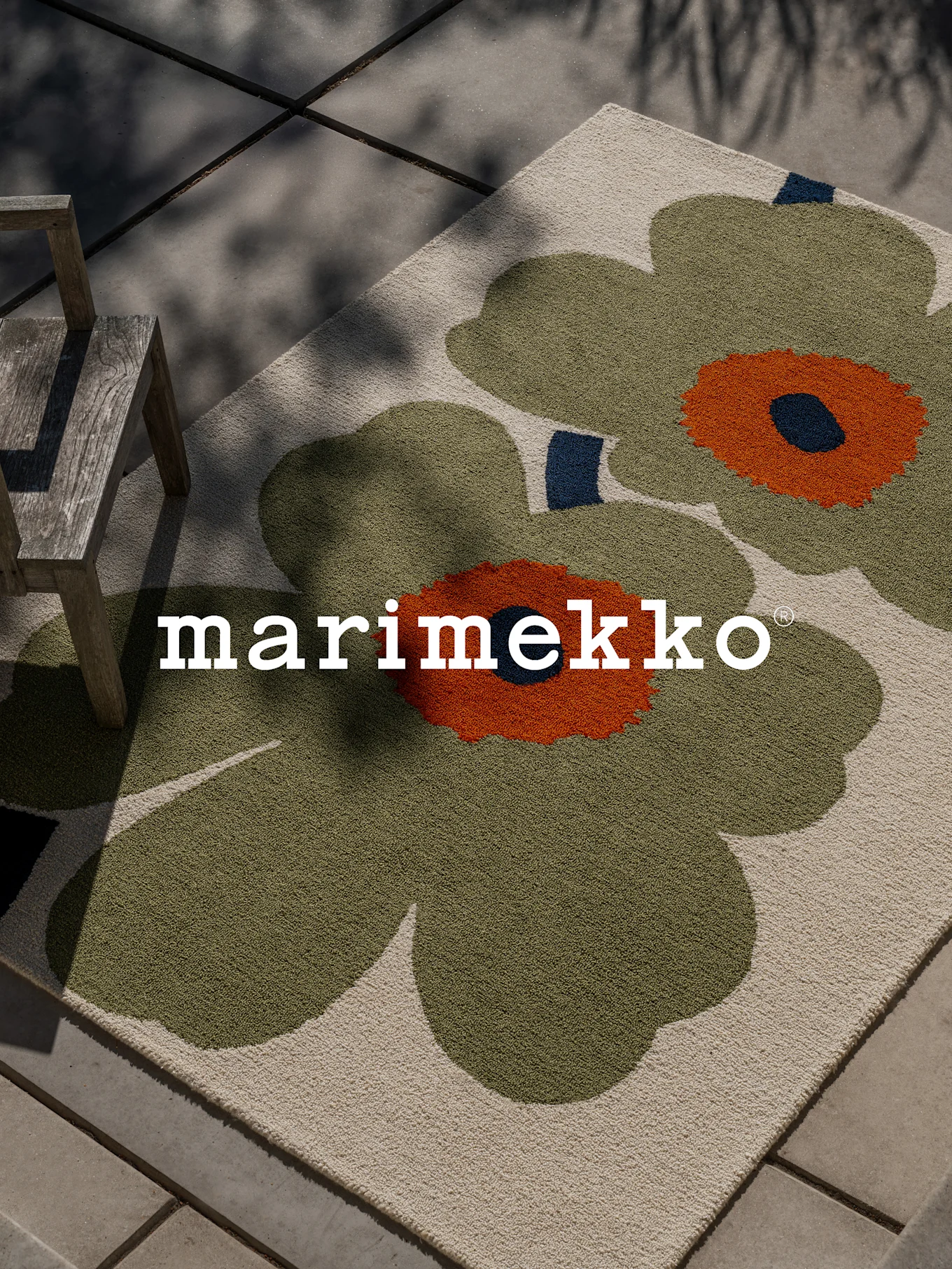 Alfombra Marimekko con gran patrón floral verde y naranja en un patio con silla de madera.