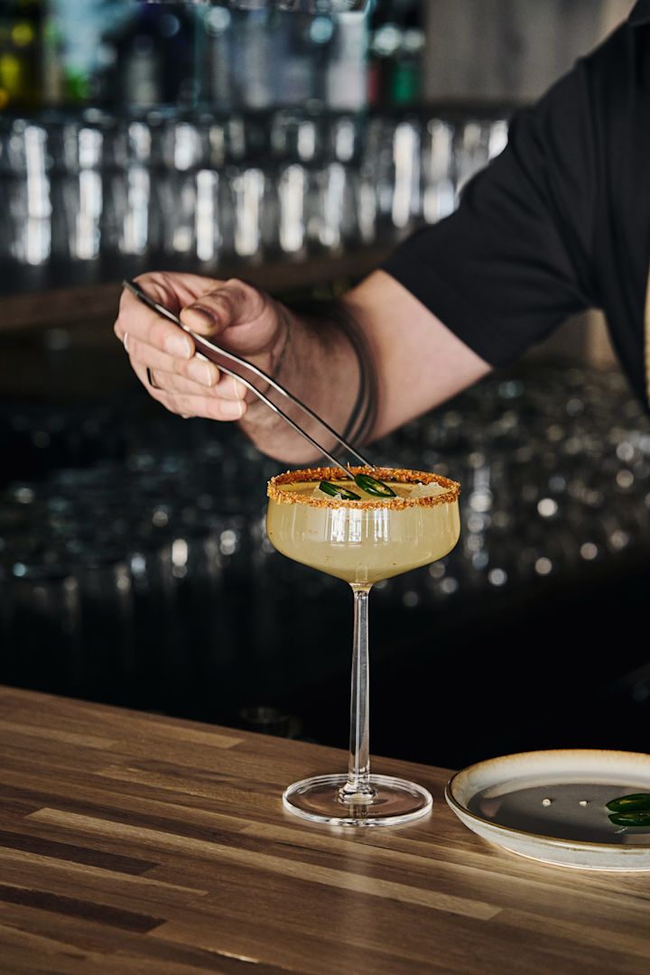 Perfectas para cócteles sin alcohol: las copas de cóctel Essence de Iittala con bebida, borde decorado y adornadas con rodajas de jalapeño con pinzas.