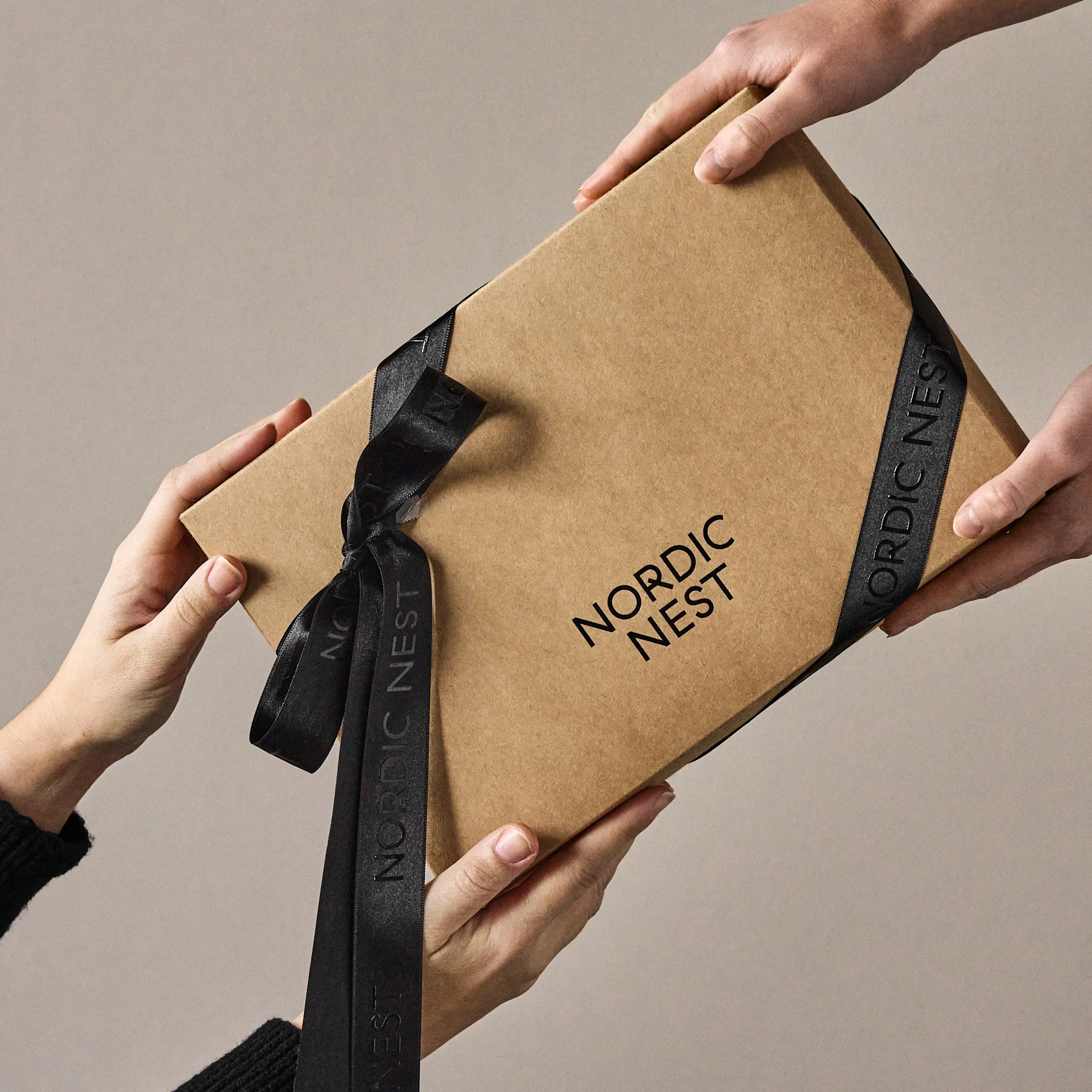 Manos intercambiando una caja de regalo marrón con el logo 'Nordic Nest' y cinta negra.