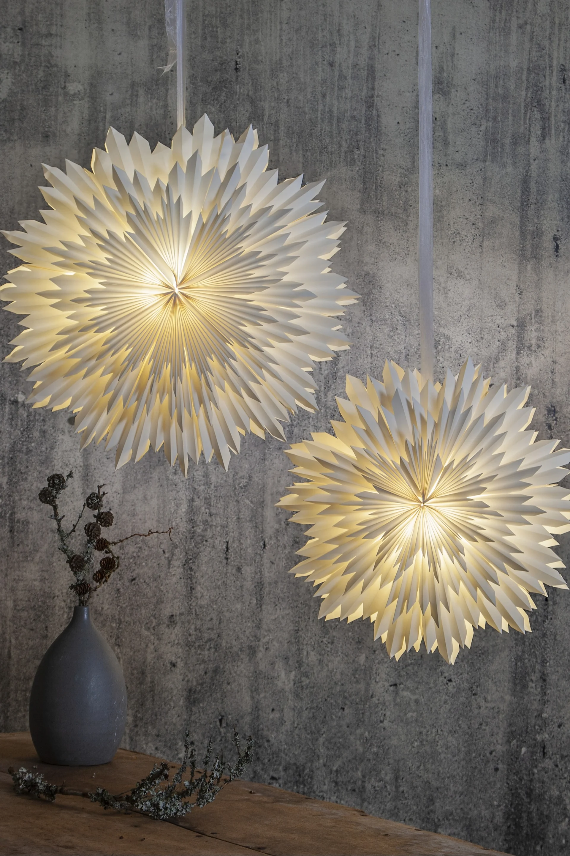 La estrella de Navidad Ice de Star Trading cuelga en pareja frente a una pared gris.