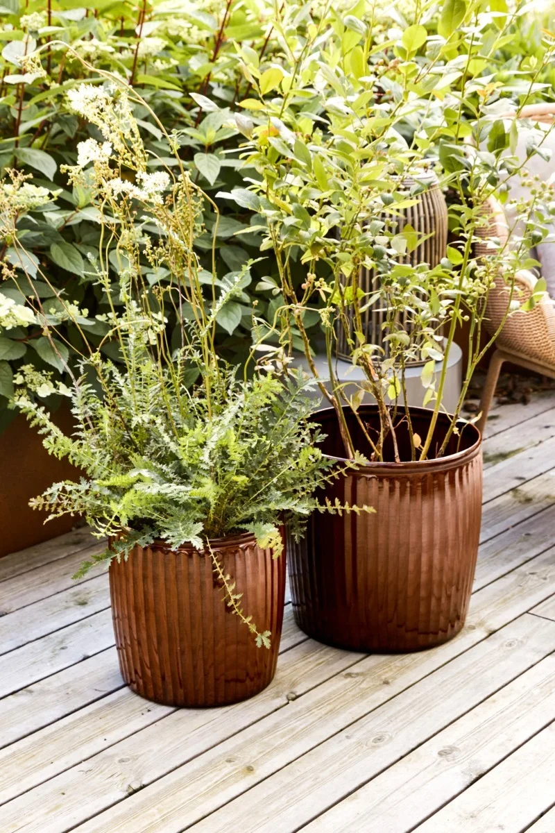 Los tonos marrones son muy adecuados para un balcón boho. Aquí puedes ver las dos macetas Groove de House Doctor con flores en un balcón.