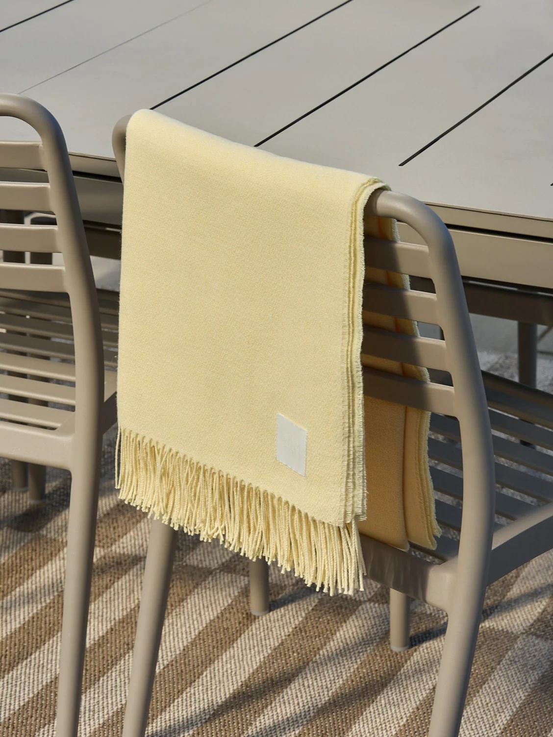 Manta amarilla clara con flecos sobre una silla de exterior beige.