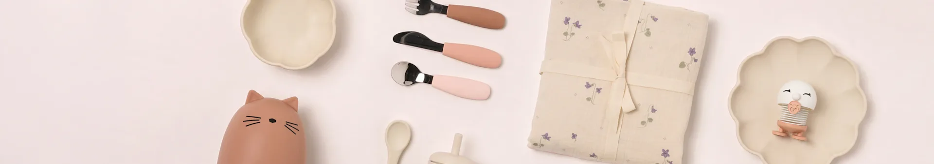 Diseño plano de artículos de comedor para bebé: platos beige, botella de gato, cubiertos rosas, manta floral, juguete de huevo.